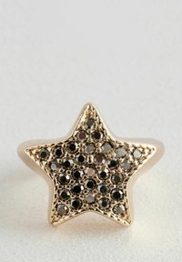Anello a forma di stella in oro con una superficie texturizzata e decorato con cristalli neri, creando un motivo scintillante.