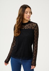 Haut noir à manches longues en dentelle avec un motif floral. Présente un corps noir uni et des manches en dentelle transparente. Détail d'ourlet festonné.