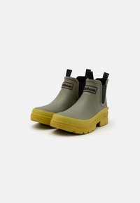 Bottines en caoutchouc grises avec une semelle jaune, présentant une texture lisse, des panneaux latéraux élastiques et un logo à l'avant.