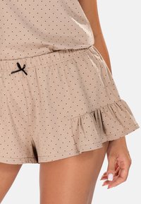 Beige šortky s černými puntíky, elastický pas, detail se šňůrkou a volánkový lem. Vyrobeno z měkké, lehké tkaniny.