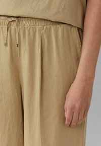 Lichtbruine linnenmixbroek met een elastische tailleband en trekkoord, zachte textuur en zijplooien voor comfort en bewegingsvrijheid.