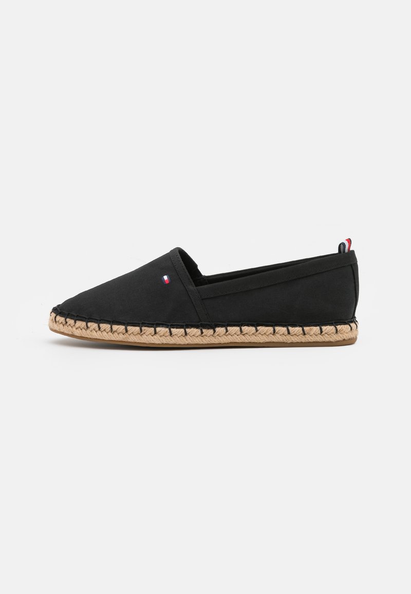 Chaussure slip-on en toile noire avec un bout pointu, détails en corde de jute le long de la semelle et un petit logo tricolore près du talon.