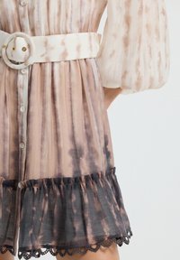 Abito leggero con strisce verticali tie-dye in beige, taupe e viola. Presenta una vita cintata bianca, chiusura con bottoni e orlo arricciato.