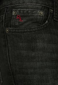 Černé denimové džíny s zadní kapsou, na které je vyšívané R.L. v červené barvě a stříbrný kovový doplňek pro zapínání. Textura je hladká s mírným leskem.