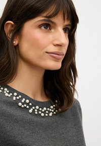 Šedý svetr s kulatým výstřihem, zdobený shluku bílých perel podél límce, hladká textura a středně těžká pletenina.