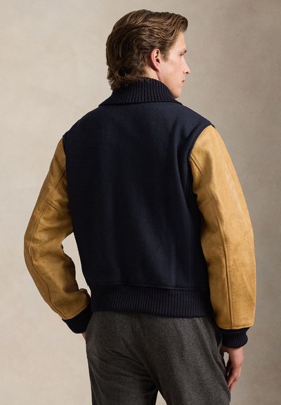 Ναυτικό σακάκι με μείγμα μαλλιού και μπεζ δερμάτινα μανίκια, ριμπ κολάρο και στρίφωμα. Διαθέτει εφαρμοστή σιλουέτα και υφασμένες δερμάτινες λεπτομέρειες.