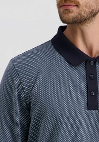 Marineblaue Polohemd mit strukturiertem Muster, ausgestattet mit einem dunklen Kragen und einer Knopfleiste mit drei Knöpfen, geeignet für die Freizeit.