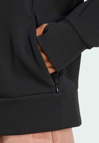 Felpa nera con cappuccio, dotata di tasca con zip, texture morbida, polsini a coste e orlo con vestibilità rilassata.