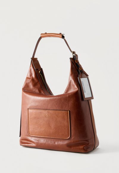 Sac fourre-tout en cuir marron avec poche avant, compartiment principal large à fermeture éclair, poignée rembourrée et étiquette Moschino attachée.