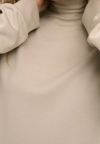 Vêtement à col roulé beige en tissu lisse. Comprend des manches longues avec une coupe décontractée, mettant en valeur un design simple et épuré.