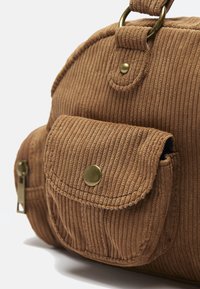 Brun kordfløjls taske med en buet form, udstyret med en frontlomme, messingbeslag og en tekstureret ribbet overflade. Inkluderer lynlåsdetalje.