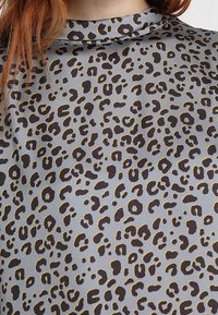 Blusa gris con estampado de leopardo en marrón oscuro y acentos en amarillo, textura suave y diseño de cuello alto.