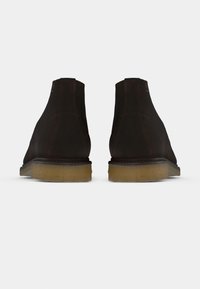 Paire de bottines en daim brun foncé avec semelles en crêpe beige clair, vues de dos sur un fond blanc.