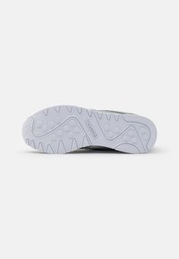 Suela de una zapatilla Reebok con un patrón de agarre texturizado y el logotipo centrado en la suela de goma blanca contra un fondo liso.