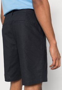 Laivastonsiniset shortsit, jotka on valmistettu teksturoidusta kankaasta. Ne ovat puhtaan muotoilun omaavat, takataskut ja suora helma, ja ne sopivat rentoon käyttöön.