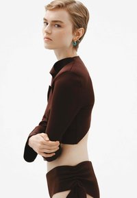 Top corto marrón con mangas largas y cuello alto, combinado con una parte inferior de cintura alta a juego que presenta detalles arrugados.