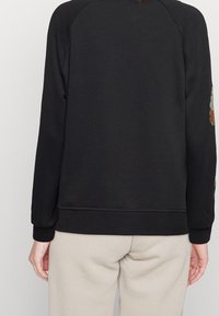 Sudadera negra con mangas raglán, puños y dobladillo acanalados. Presenta bordados florales en la manga derecha. Tejido suave y texturizado.