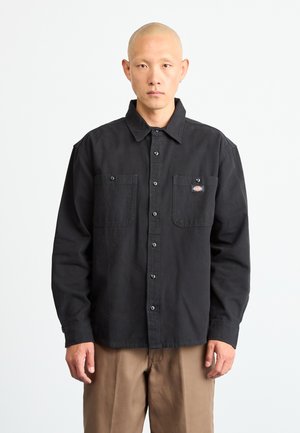 Black button-up shirt made of cotton with two chest pockets, contrasting buttons, and a small logo patch on the left pocket.