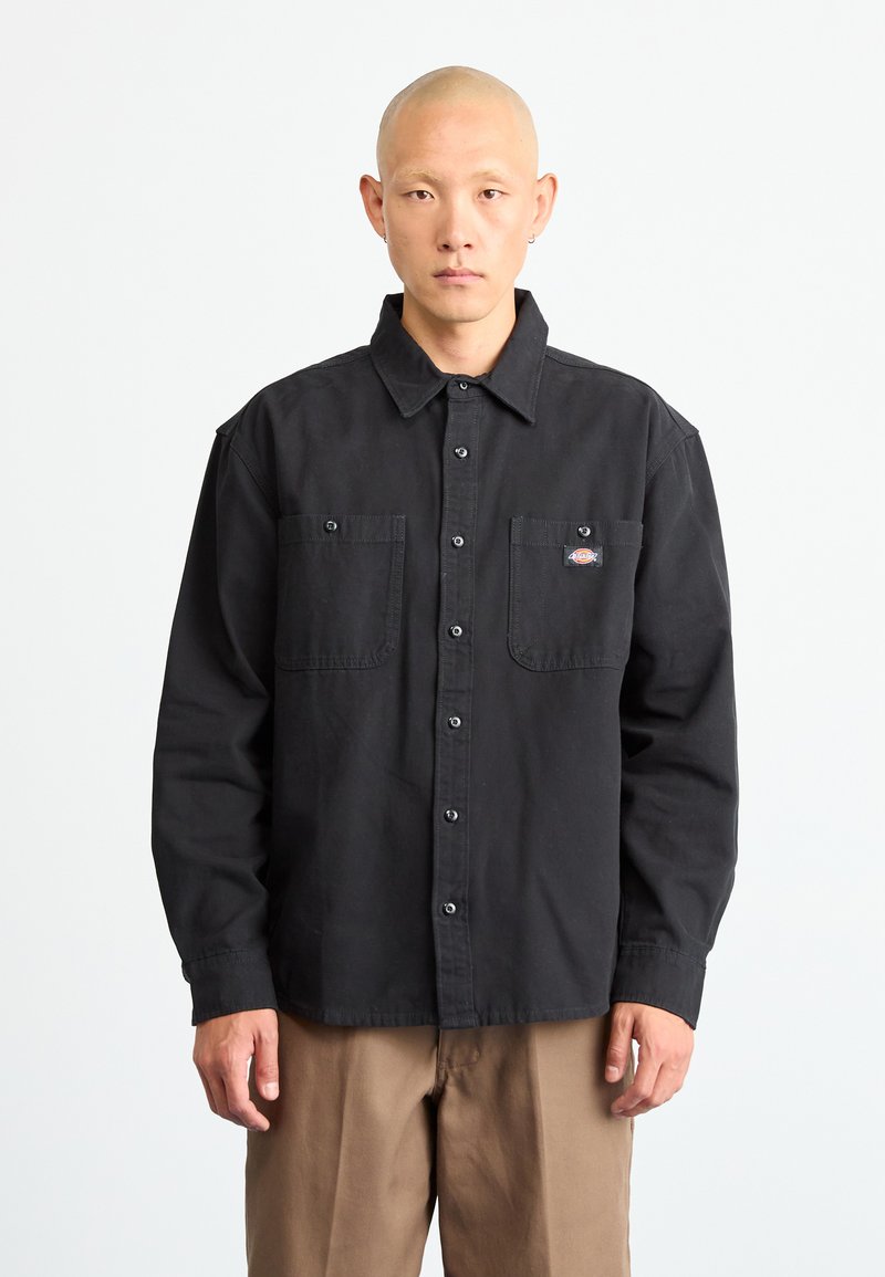 Black button-up shirt made of cotton with two chest pockets, contrasting buttons, and a small logo patch on the left pocket.