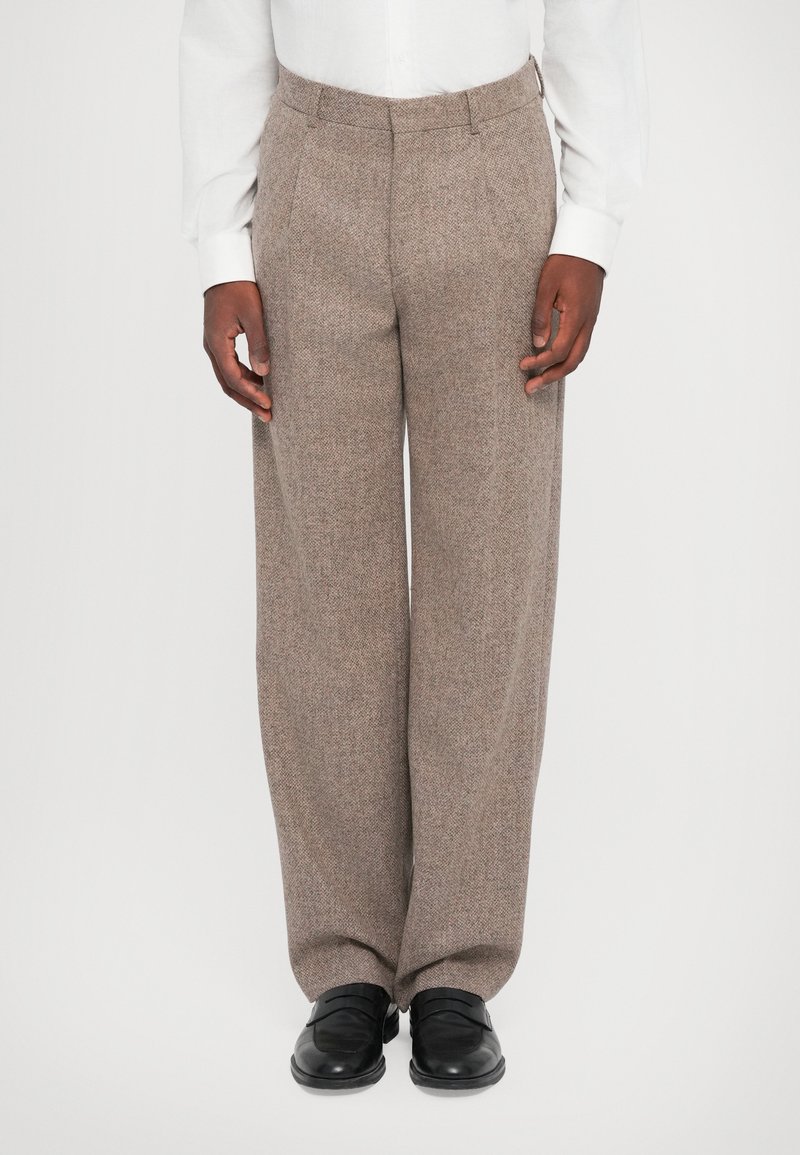 Pantalons en chevron marron avec une coupe décontractée, fabriqués en tissu texturé. Associés à des chaussures noires, avec une conception à l'avant plat.