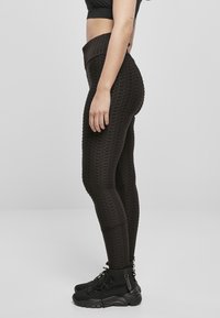 Leggings noires texturées avec une taille haute, présentant un motif en grille et un design ajusté. Portés avec des bottes de cheville noires à lacets.