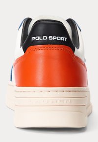 Zapatilla de cuero blanca y naranja con un talón negro, presenta la marca "POLO SPORT", superficie texturizada y una suela de goma con patrón.