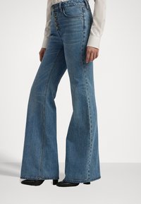 Lys blå slengbukser laget av denim med høy midje, med fem-knaps lukking, tonalt søm og rå kanter.