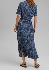 Robe maxi bleue à motif floral, avec manches courtes, taille ceinturée et fentes latérales. Confectionnée dans un tissu léger avec un motif floral texturé.