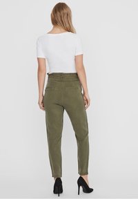 Pantalones de color verde oliva con cintura alta, piernas ajustadas y dos bolsillos traseros, combinados con una camiseta blanca de manga corta y tacones negros.