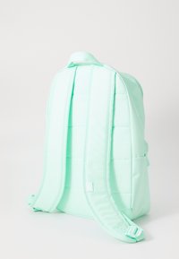Mochila verde menta com tecido acolchoado, apresentando alças duplas ajustáveis e bolsos laterais. Textura suave, design minimalista.