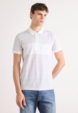 Weißes Polohemd mit Karomuster, kurzen Ärmeln und Kragen. Mit einem Logo auf der Vorderseite und kombiniert mit hellblauen Jeans.