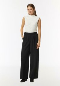 White sleeveless top with textured zigzag pattern, paired with high-waisted black wide-leg trousers. Smooth fabric, minimalist design.
