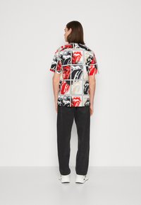 Camisa de manga corta con un diseño gráfico multicolor que presenta labios y acentos en rojo, negro y blanco, confeccionada en tela suave.