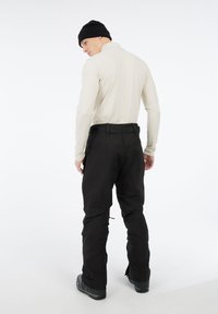 Zwarte outdoor broek met een relaxte pasvorm, gecombineerd met een lichtbeige langemouwen top. Kenmerken zijn een effen kleur en minimale hardware.