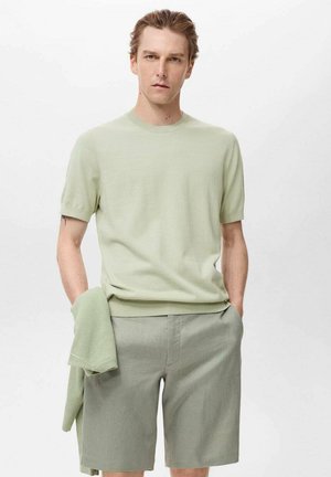 Hellgrüner Strickpullover mit kurzen Ärmeln und rundem Halsausschnitt, kombiniert mit hellgrünen Shorts. Ein passender gefalteter Pullover liegt über dem Arm.