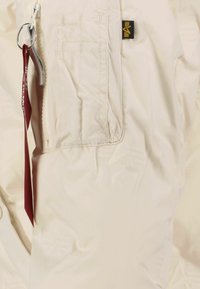 Helle, gepolsterte Jacke mit einem Reißverschlussfach, Stoffetikett-Detail und glatter, glänzender Textur. Schlüsselring-Akzent in der Nähe des Reißverschlusses.