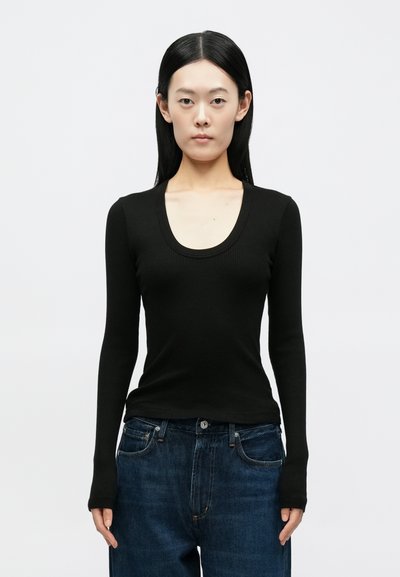 Μαύρο μακρυμάνικο ριμπ μπλουζάκι με στρογγυλή λαιμόκοψη, συνδυασμένο με ψηλόμεσα μπλε τζιν παντελόνια. Ομαλή υφή, εφαρμοστή γραμμή.