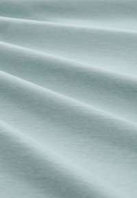 Jasnoniebieska bawełniana tkanina o gładkiej fakturze, z fałdami tworzącymi subtelne cienie i głębię. Drobno tkana, miękka w wyglądzie.