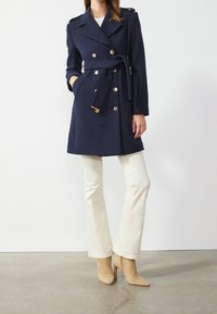Granatowy wełniany płaszcz dwurzędowy z złotymi guzikami, paskiem w talii, naramiennikami i bocznymi kieszeniami. Połączony z kremowymi spodniami w stylu dzwonów i beżowymi szpilkami.