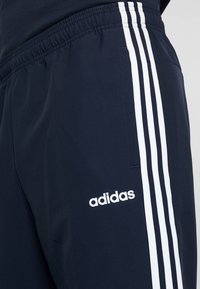 Navy Jogginghose aus weichem Stoff, mit einem weißen Drei-Streifen-Design an den Seiten und einem weißen Adidas-Logo auf dem Oberschenkel.