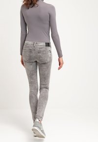 Jeans ajustados grises con una textura desgastada y un ligero desvanecimiento, con bolsillos traseros y una etiqueta negra. Combinados con zapatillas grises.