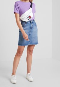 Maglietta viola in cotone, marsupio bianco con logo, gonna a matita in denim blu, sneakers bianche. Design semplice, abbigliamento casual.