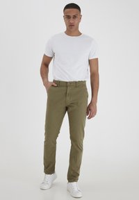Khaki chinos uskog kroja s prednjim džepovima, u kombinaciji s običnom bijelom majicom s okruglim izrezom i bijelim tenisicama.