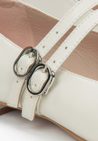 Białe skórzane buty z podwójnymi paskami i srebrnymi klamrami. Gładka tekstura i niski obcas. Wnętrze w jasnym odcieniu.