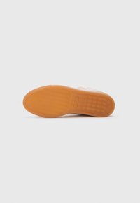 Suela de una zapatilla casual blanca con una suela de goma que presenta un diseño de banda para mejorar el agarre, sobre un fondo blanco liso.