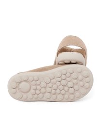 Beige suede sandal with a rounded toe, elastic strap, and a textured rubber sole featuring small raised dots for grip.