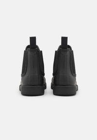 Black ankle boots with elastic side panels, textured rubber material, and pull tabs at the back for easy wear. Sturdy black rubber soles.