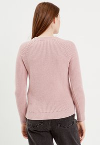 Roze gebreide trui met ribbeltextuur, lange mouwen en een ronde halslijn, met een aansluitende tailleband en raglanmouwontwerp.