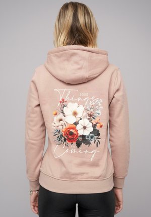 Light pink hoodie with a floral design on the back, featuring white, red, and blue flowers alongside text that reads "Good Things Are Coming."