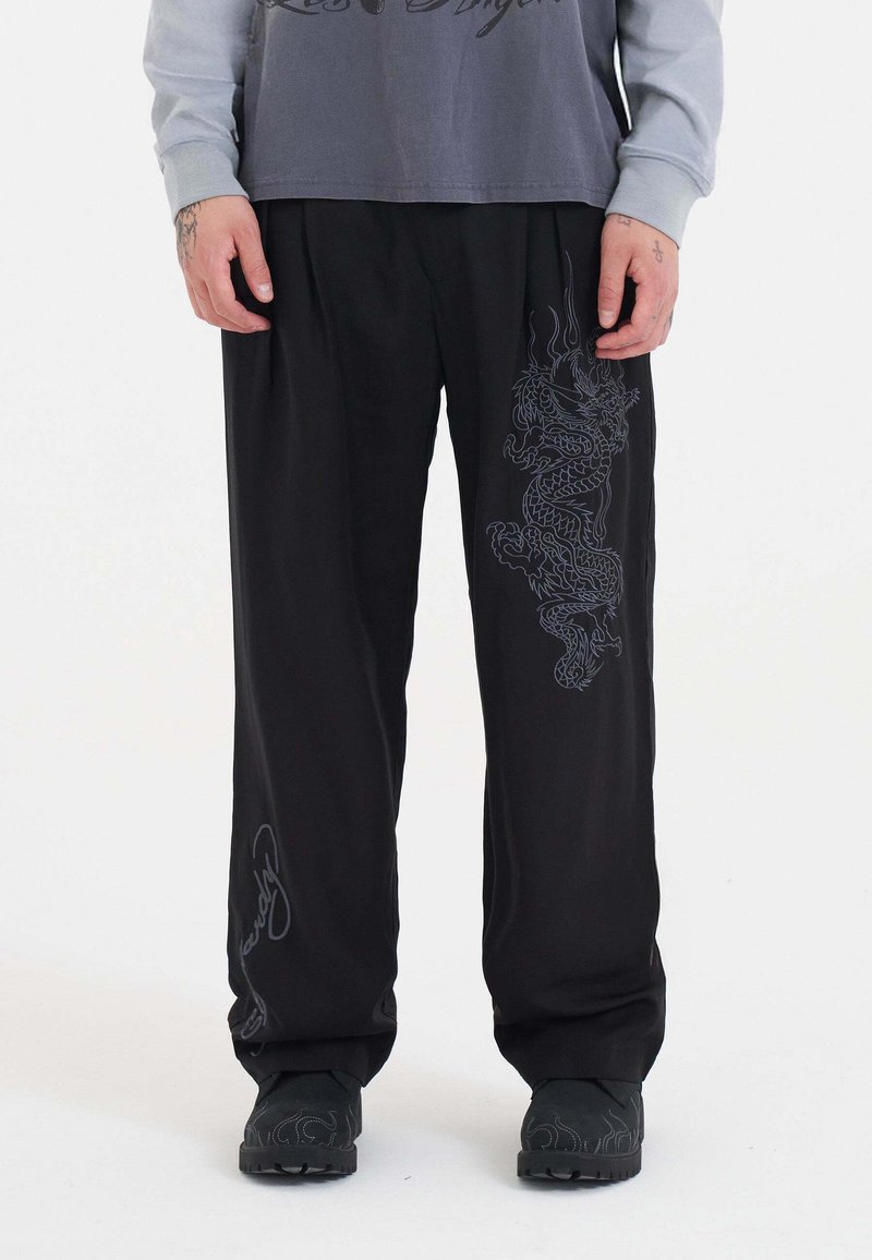 Zwarte relaxed-fit broek met een drakenontwerp in donkergrijs op één been en merktext op het andere been, gemaakt van een gladde stof.